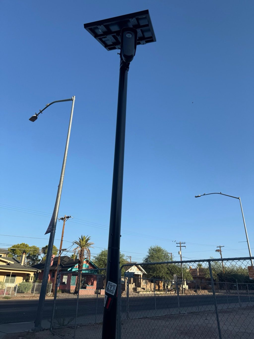 blue sky background with light pole and black fence, ALPR camera on top of a black pole with solar panel is front and center